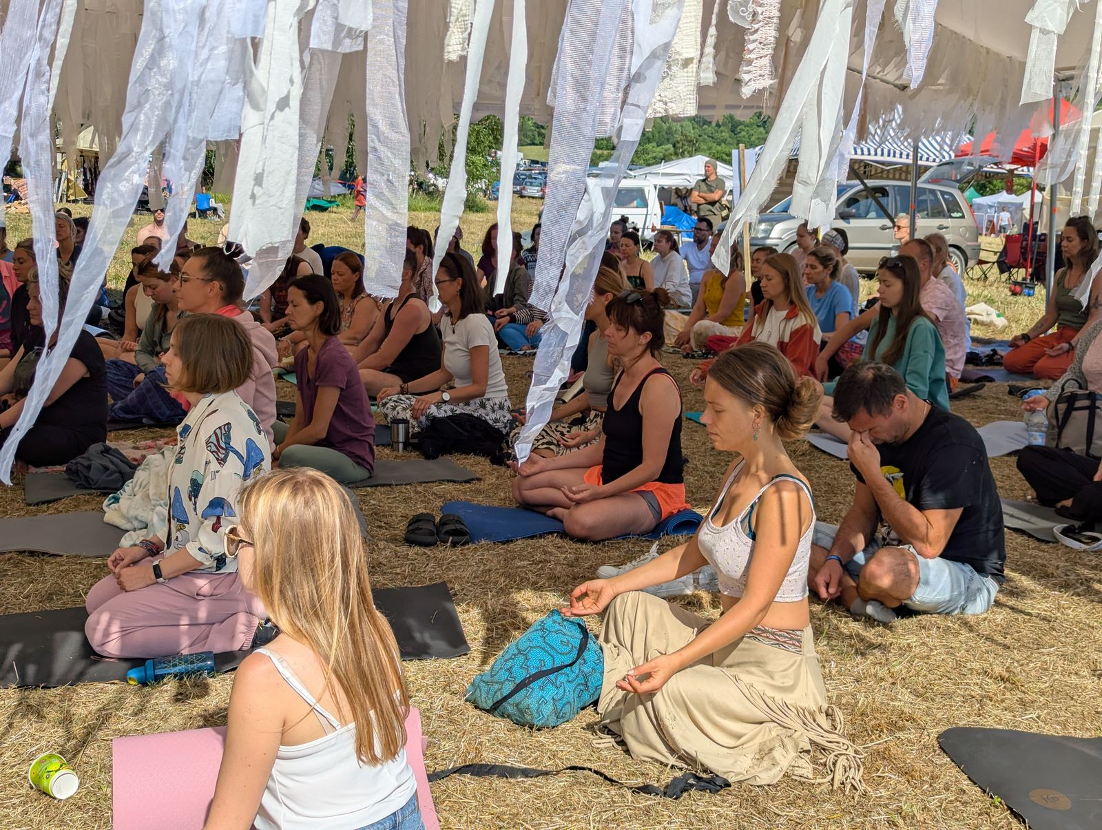 Duża grupa medytująca pod namiotem na festiwalu
